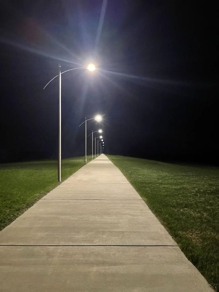 Uma rua vazia de noite sem nada ao redor além de grama e postes ao longo da rua
